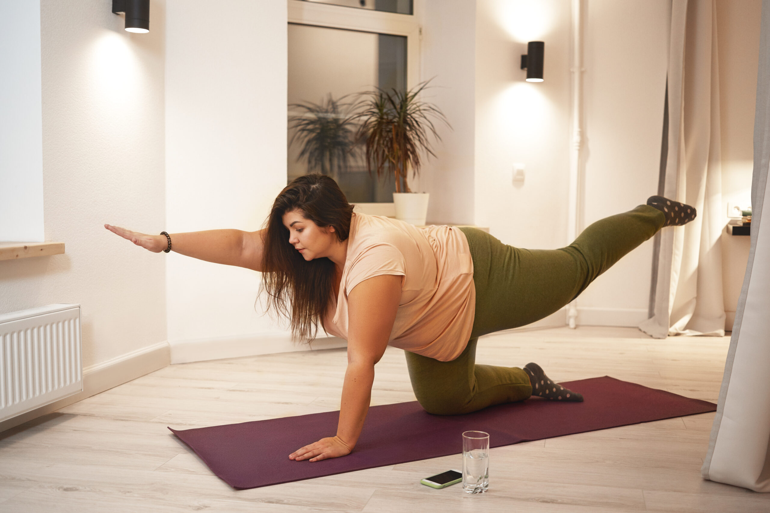 Mulher praticando yoga em sua casa, fortalecendo um hábito saudável.